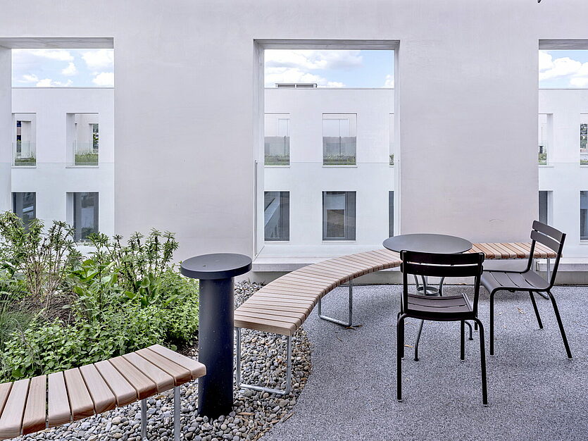 Terrasse mit Rundbank, Tisch und Pflanzen vor weisser Fassade im JED Schlieren