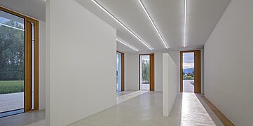 Heller Innenraum mit weißen Wänden, großen Fenstern und LED-Beleuchtung. Minimalistisches Design.