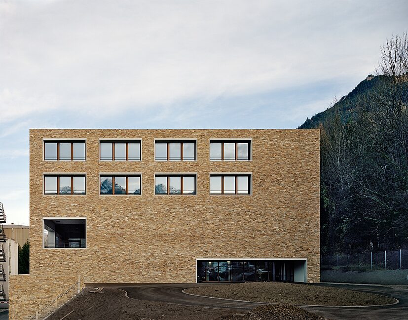 Ein architektonisches Statement für die Marke Hilti Kubisches Backsteingebäude mit klarer Fensterstruktur vor bewaldeter Hügellandschaft