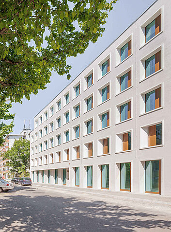 Auszeichnung Zwei Personen spazieren in einer ruhigen Stadtstraße mit modernen, hellen Fassaden