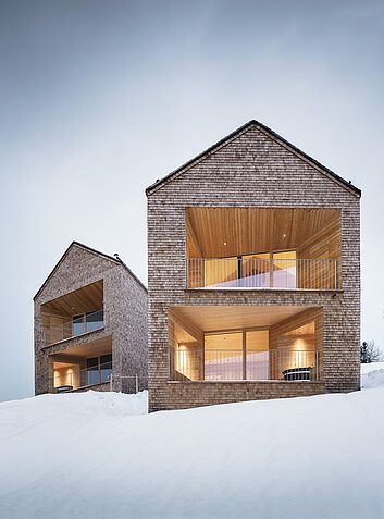 Auszeichung Zwei moderne Holzchalets mit großen Fensteröffnungen in verschneiter Winterlandschaft